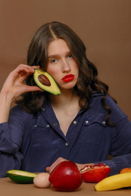 Young woman in group of fruit Healthcare and healthy nutrition concept holds avocado to face