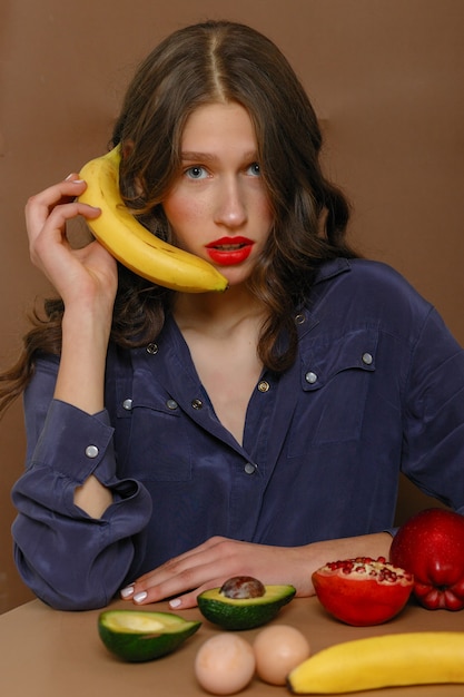 Young woman in group of fruit. Healthcare and healthy nutrition concept. sitsspeaks into a banana like a phone