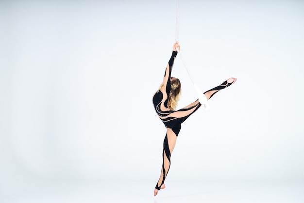 Young woman gymnast wearing black costume on trapeze on white.