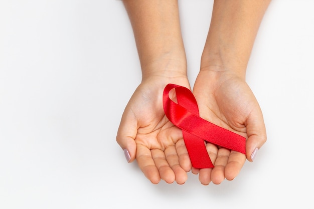 Young woman hand holding red ribbon, with background. AIDS prevention