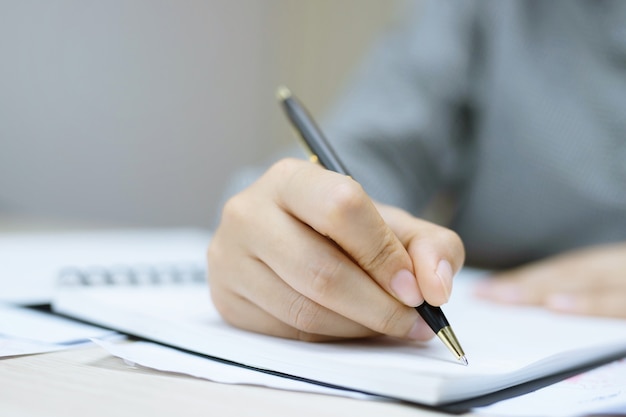 Young woman hands hold opened notebook pages with blue pencil in light wooden table with bookmarks