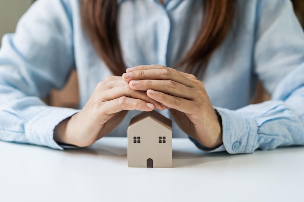 Young woman hands protecting miniature house Home insurance concept