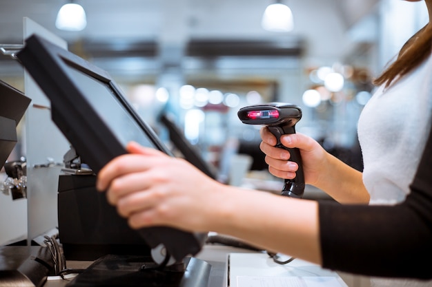 Young woman hands scaning / entering discount / sale on a receipt, touchscreen cash register, market / shop