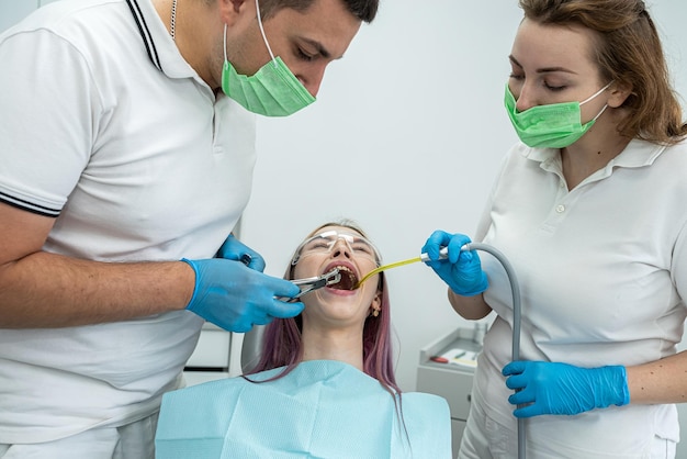 Young woman has her teeth treated by a male dentist and a female assistant during an appointment at a dental clinic dentistry teeth