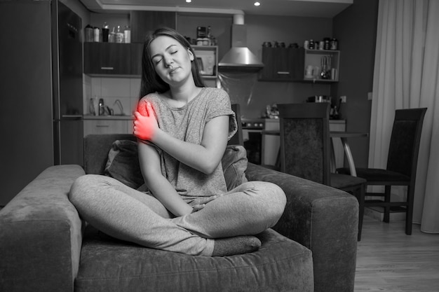 Young woman has shoulder pain, black and white photo red accent