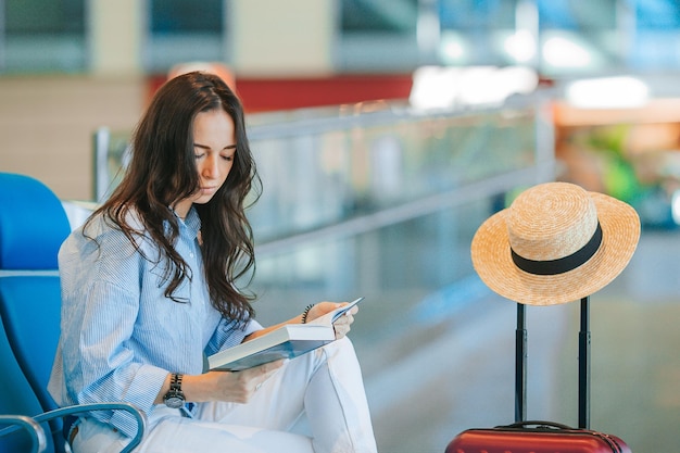 Young woman in hat with baggage in international airport walking with her luggage