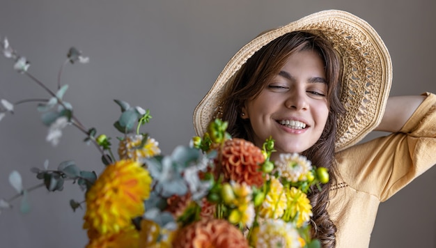 Young woman in a hat with a bouquet of chrysanthemums on a gray background