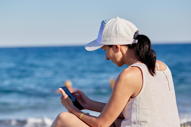 Young woman in a hat with a phone on the beach near the sea The concept of freelancing working online online conference or studying online High quality photo