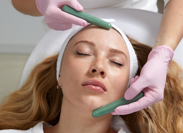 Young woman having facial massage with stone sticks in spa salon