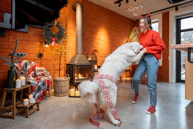 Young woman having fun dancing with her cute white dog during a happy New Year holidays by a fireplace at home