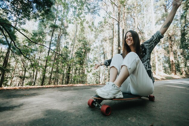 Young woman having fun descending a road in the middle of the forest with a longboard skate Practicing outdoors and extreme sports far away from the city New generations and freedom concept