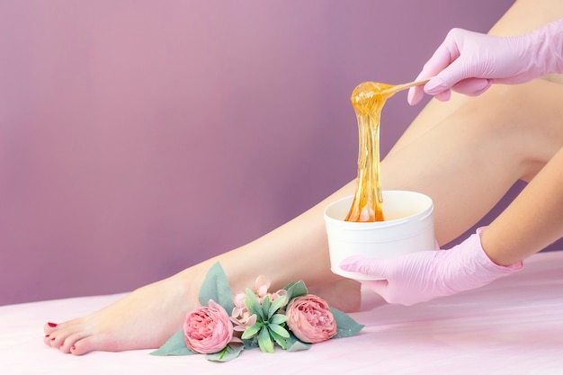 Young woman having hair removal procedure on leg with sugaring paste in salon