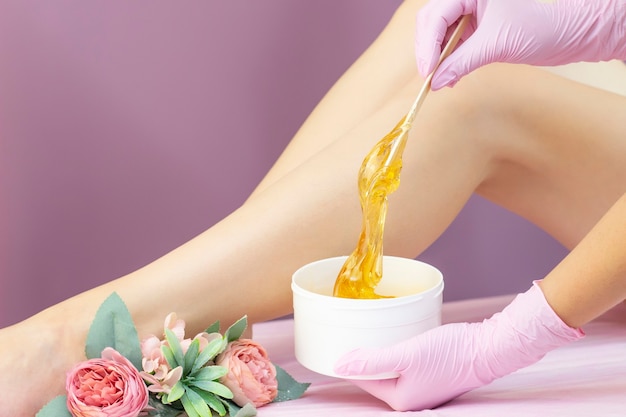 Young woman having hair removal procedure on leg with sugaring paste in salon