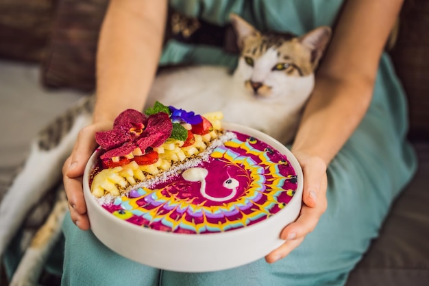 Young woman having a mediterranean breakfast seated at her sofa and with her cat and eats healthy