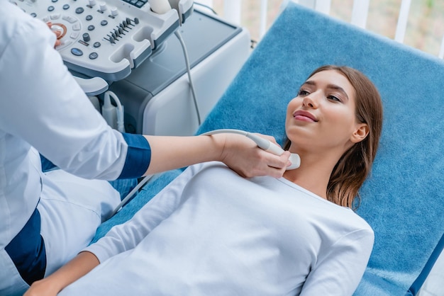 Young woman having neck ultrasound scanning examination by her doctor in modern clinic