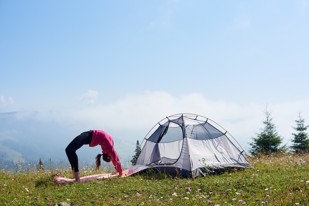 Young woman having a rest near tourist tent in the summer morning in the mountains