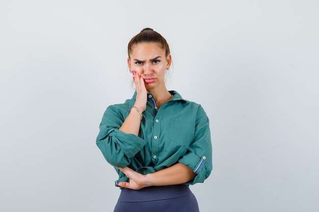 Young woman having terrible toothache in green shirt and looking gloomy. front view.