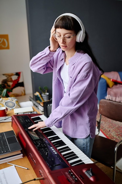 Young woman in headphones playing piano to record song during rehearsal in studio