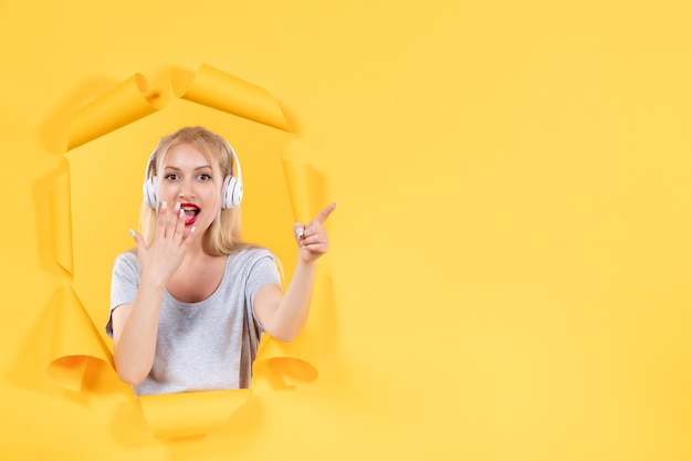 Young woman in headphones pointing at something on yellow surface