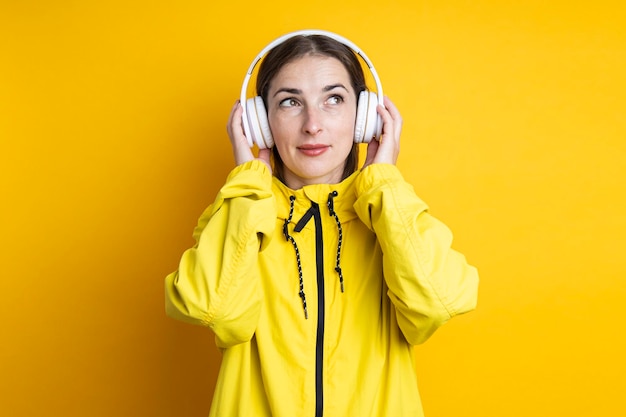 Young woman in headphones in a yellow jacket on a yellow background