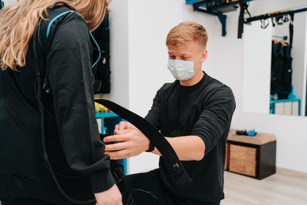 Young woman helped by her young coach while putting her in the electrostimulation suit