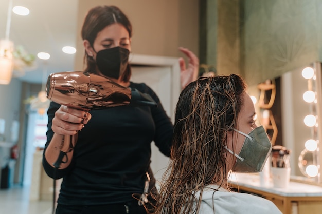 Young woman in her 30s drying the hair of a young woman in her 20s in a hairdressing salon. Horizontal