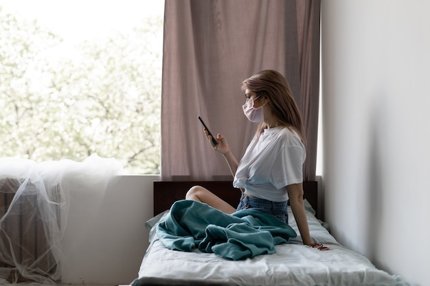 Young woman in her bed with a protective mask