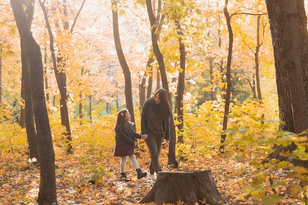 Young woman and her child girl walking through autumn park. Single parent and motherhood concept.