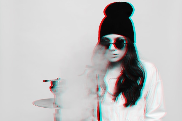 A young woman in a hipster image smokes a hookah sheesha and enjoys smoking Black and white with 3D glitch virtual reality effect