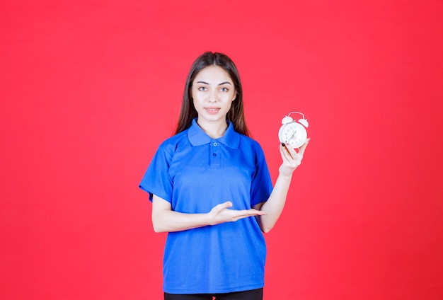 Young woman holding an alarm clock and pointing at it