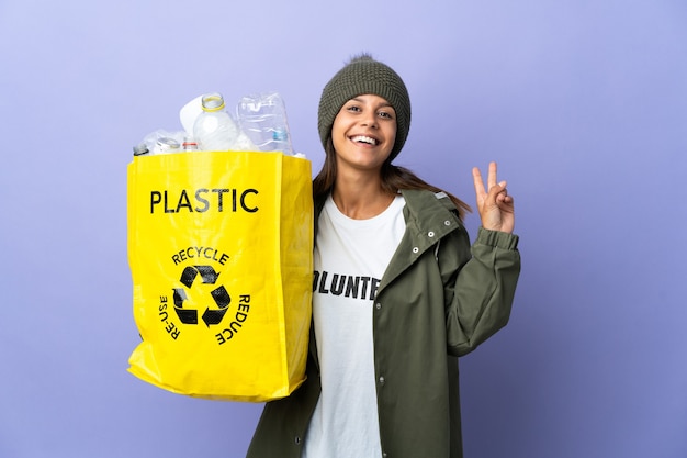 Young woman holding a bag full of plastic smiling and showing victory sign