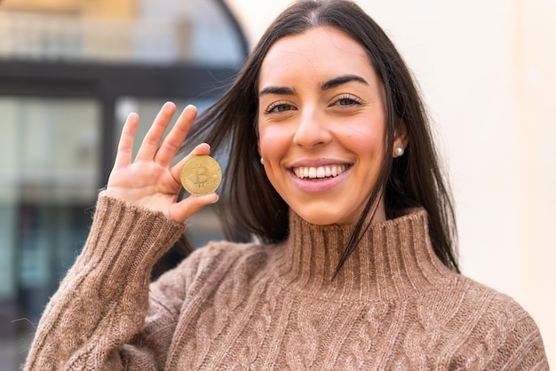 Young woman holding a Bitcoin at outdoors with surprise and shocked facial expression