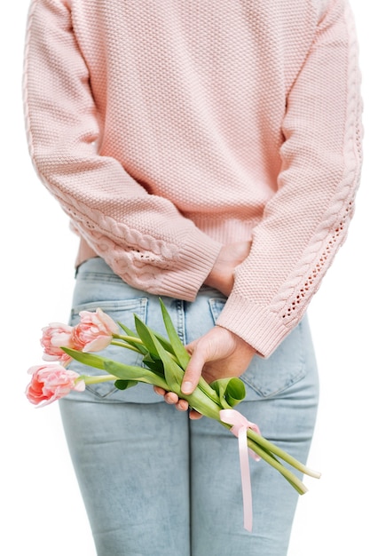 Young woman holding a bouquet of pink tulips behind her back on a white background. Text space, selective focus.