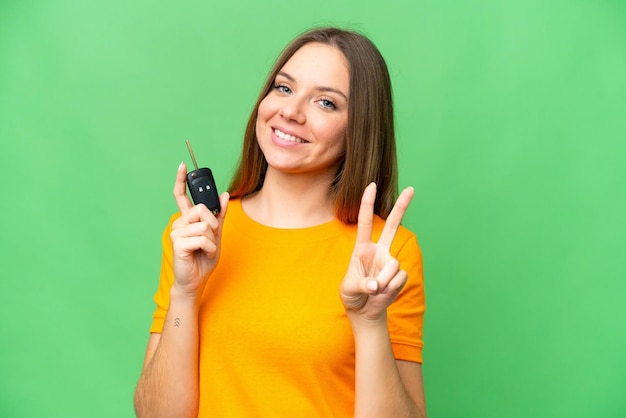 Young woman holding car keys over isolated chroma key background smiling and showing victory sign