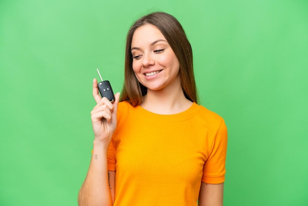 Young woman holding car keys over isolated chroma key background with happy expression