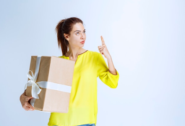 Young woman holding a cardboard gift box and thinking about the unknown sender