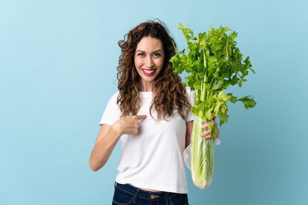 Photo young woman holding a celery isolated on blue wall with surprise facial expression