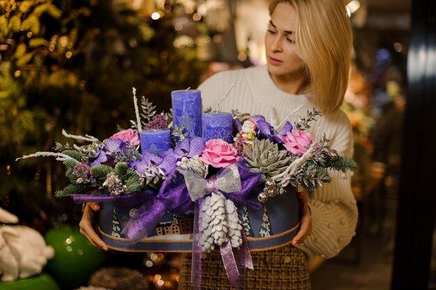 Young woman holding a christmas composition with purple and pink flowers, succulents, fir-tree branches and candles