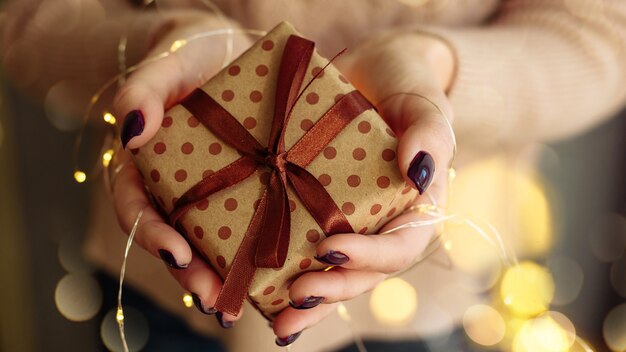 Young woman holding a Christmas present with garland lights