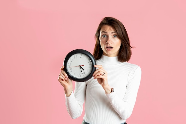 Young woman holding a clock on a pink background