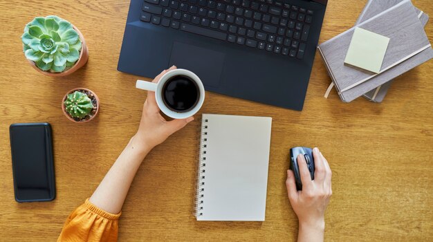 young woman holding a coffee cup and using a laptop computer on a wooden desk