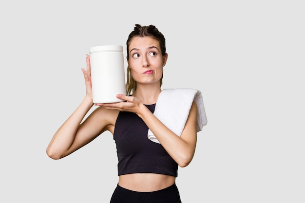 Young woman holding a container of protein powder dressed in sportswear