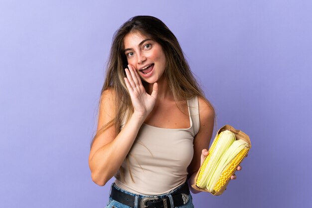 Young woman holding corn isolated on purple background whispering something