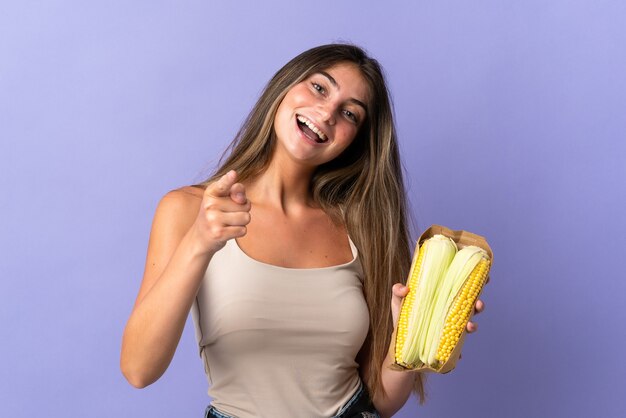 Young woman holding corn isolated on purple points finger at you with a confident expression