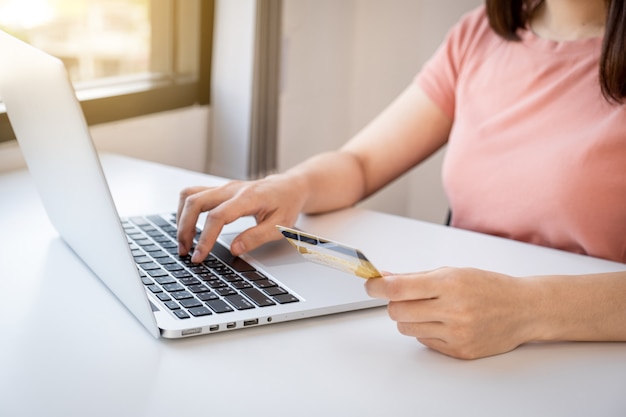 Young woman holding a credit card and typing on a laptop