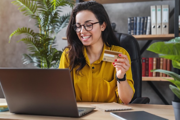 Young woman holding credit card and using laptop computer for online shopping