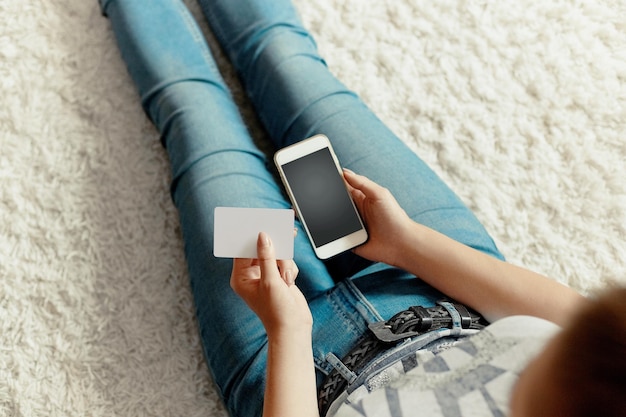 Young woman holding credit card and using phone sitting on floor Payment Online shopping concept