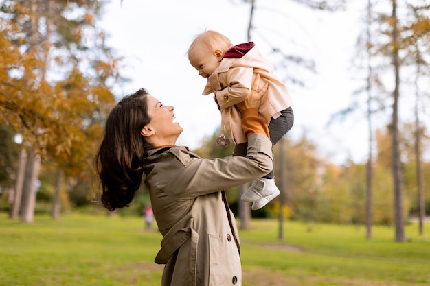 Young woman holding cute baby girl in the autumn park