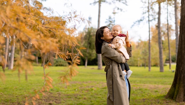 Young woman holding cute baby girl in the autumn park