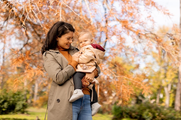 Young woman holding cute baby girl in the autumn park